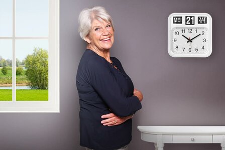 Vrouw thuis poseert voor de wand met de grote Fysic FK950 klok met duidelijke dag- en datumweergave