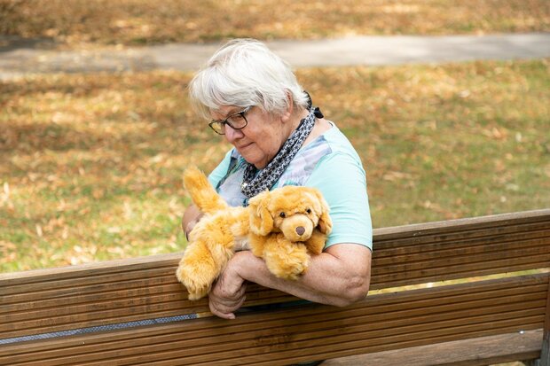 Oudere vrouw met dementie knuffelt Joyk Brando therapiehond op een bankje in het park